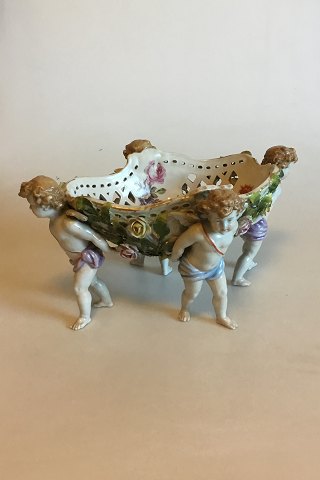 Large tableware made of porcelain, richly modeled and adorned with pousing flowers, decorated in colors and gold, carried by four putti. Plaue mark from 1916.