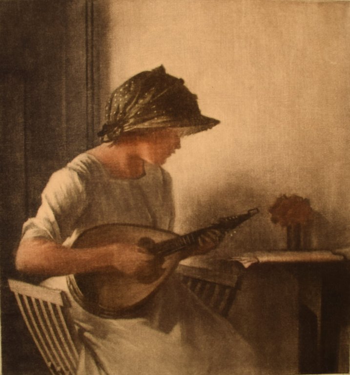 Peter Ilsted (1861-1933). Interiør med mandolinspillende ung kvinde. Mezzotinte i farver. 