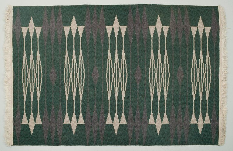 Swedish textile designer. Handwoven carpet in pure wool. Modernist design. Geometric fields in white and purple on a green background.