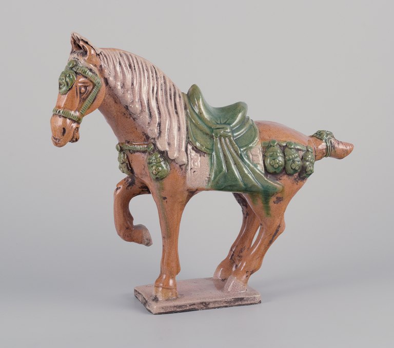Kinesisk Tang hest i lertøj.
Håndglaseret i brune og grønne nuancer.
