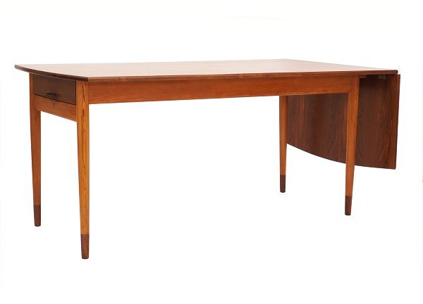 Skrivebord af Bent Moudt udført af snedkermester Arne Poulsen i fyr og palisander og præsenteret på Snedkerlaugets udstilling 1954 benævnt "Samlerens bord". H: 73cm. Plade: 160cm + 47cm (klap) x 84cm